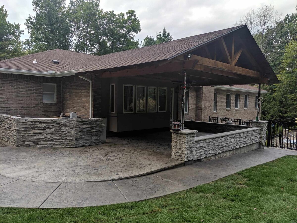 Covered outdoor living area with stamped concrete and stone walls in Central New York