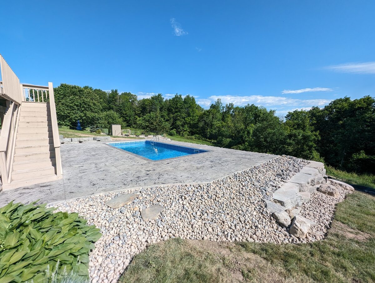 Hillside stamped concrete pool patio with stone landscaping in Central New York