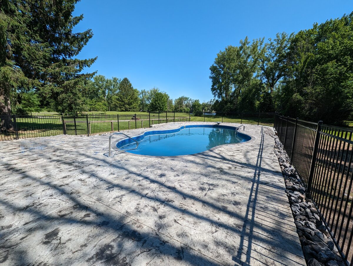Stamped concrete pool deck with black aluminum fence in Central New York