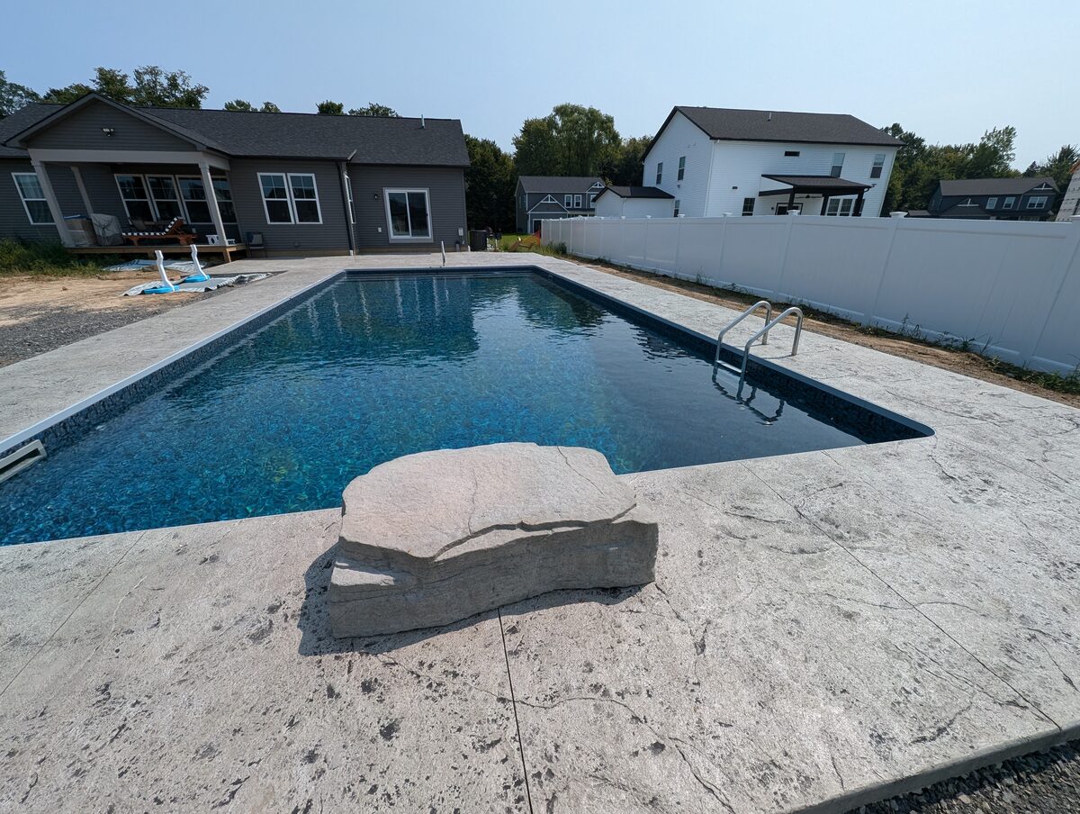 Modern stamped concrete pool deck with boulder accent in Syracuse NY