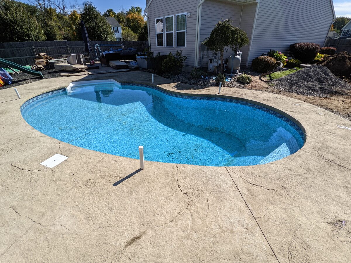 Tan stamped concrete pool deck surrounding an in-ground pool in Syracuse NY